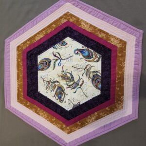 Table topper shaped like a hexagon. Fabric colors purple and gold.